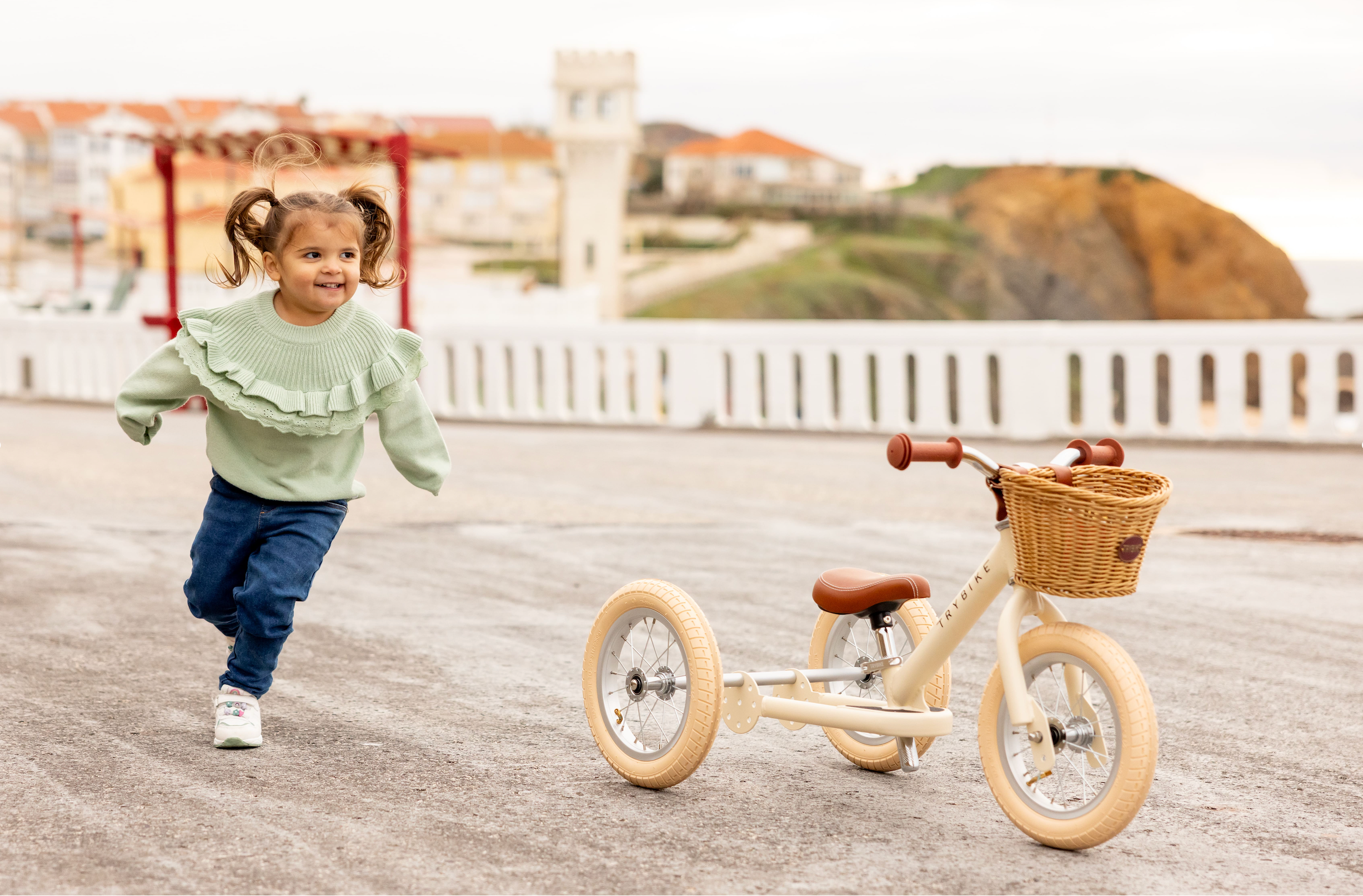 Child running with a tricycle on a paved path with a scenic background